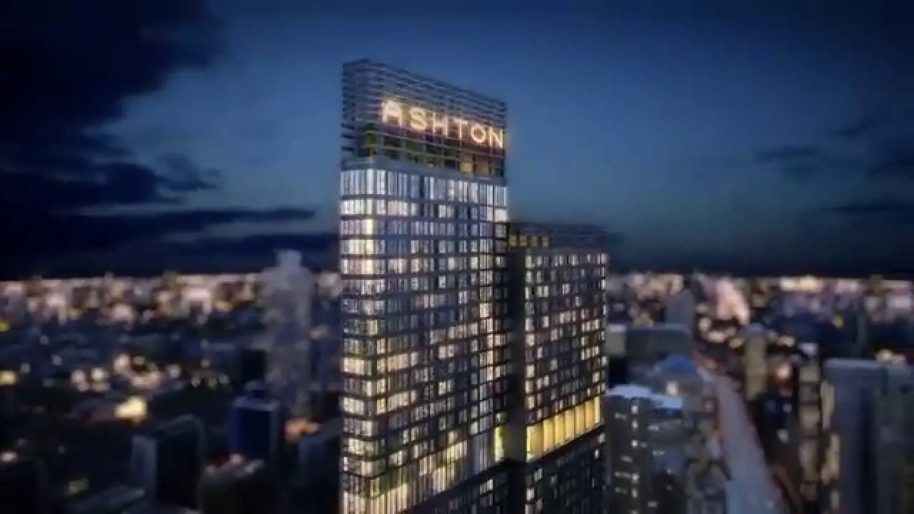 一座摩天大楼，顶部亮着“ASHTON”字样，与夜幕下的城市景观交相辉映。