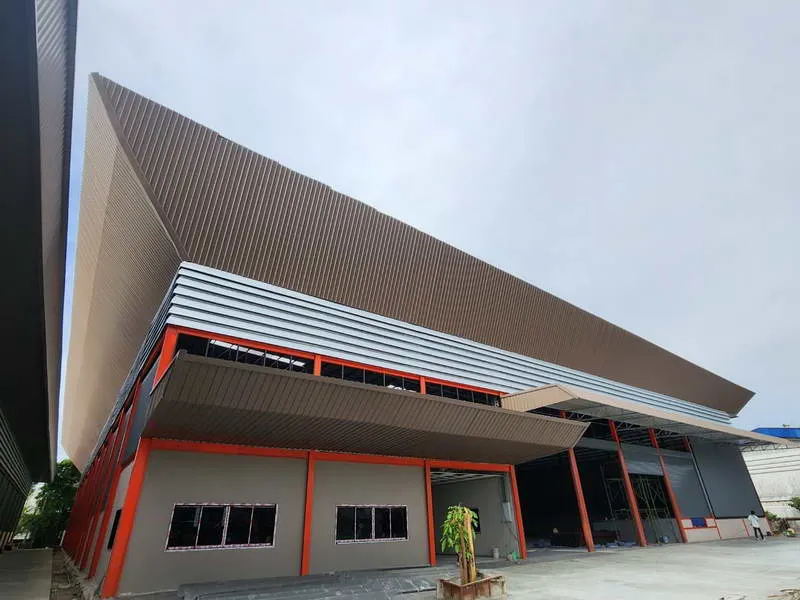 现代工业建筑，采用红色和灰色面板，设有大型金属悬挑和未完成的窗户，背景是晴朗的天空。