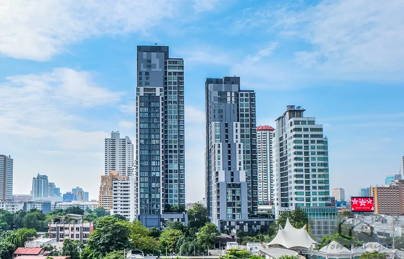 现代都市景观，高耸入云的摩天大楼在湛蓝的天空下拔地而起，周围环绕着低矮的建筑和绿地。