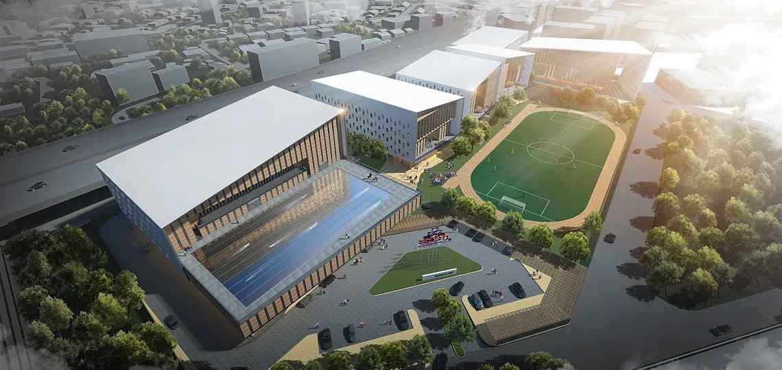Aerial view of a modern architectural complex with rectangular buildings, a football field, parking area, and surrounding greenery.