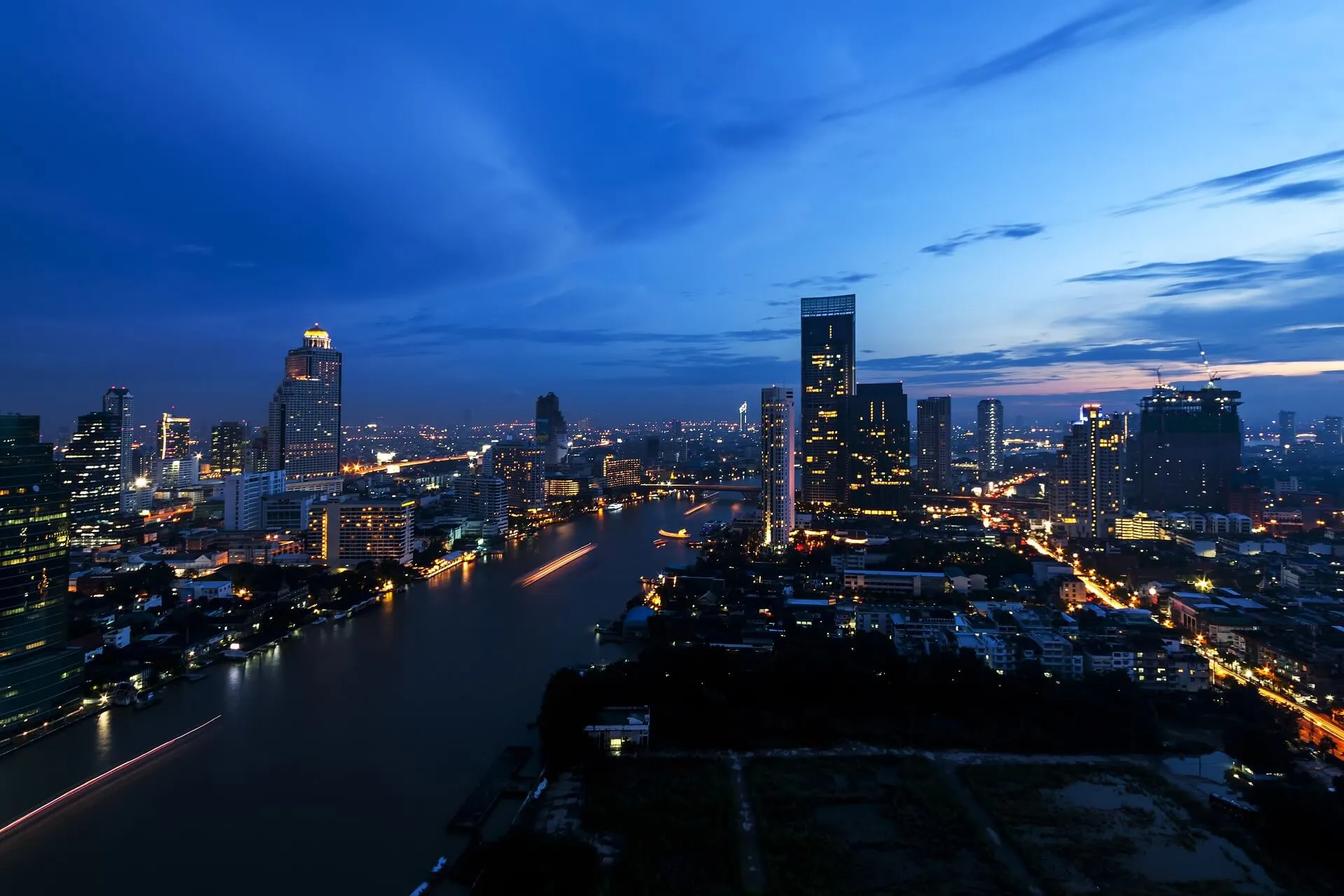 ทิวทัศน์เมืองยามพลบค่ำ อาคารต่างๆ สว่างไสว และแม่น้ำสะท้อนแสงไฟ