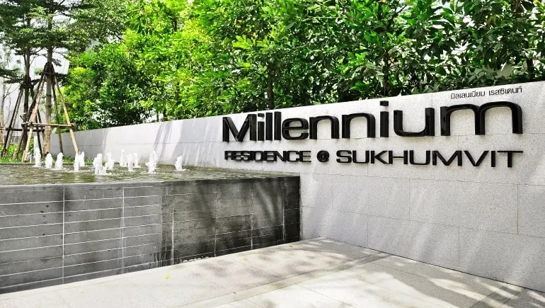 Entrance sign of Millennium Residence at Sukhumvit, surrounded by greenery and a water feature, in daytime.