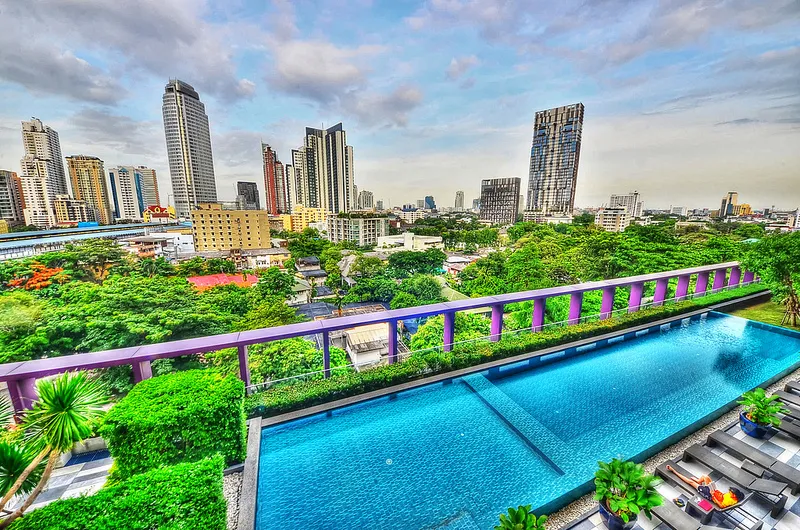 สระว่ายน้ำไร้ขอบบนดาดฟ้า มองเห็นเส้นขอบฟ้าเมืองสมัยใหม่และต้นไม้เขียวชอุ่มเป็นฉากหลั