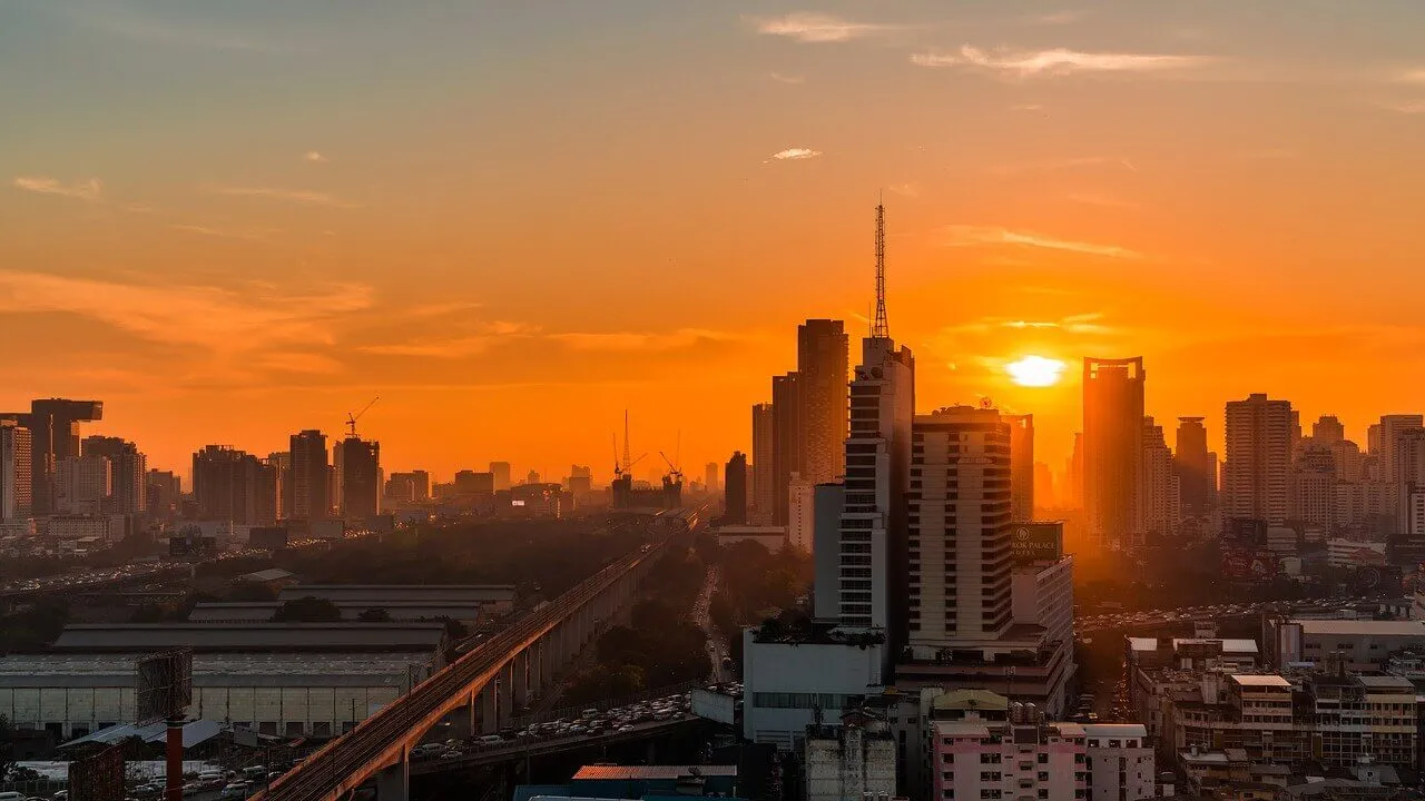 City skyline at sunset with high-rise buildings silhouetted against an orange sky.