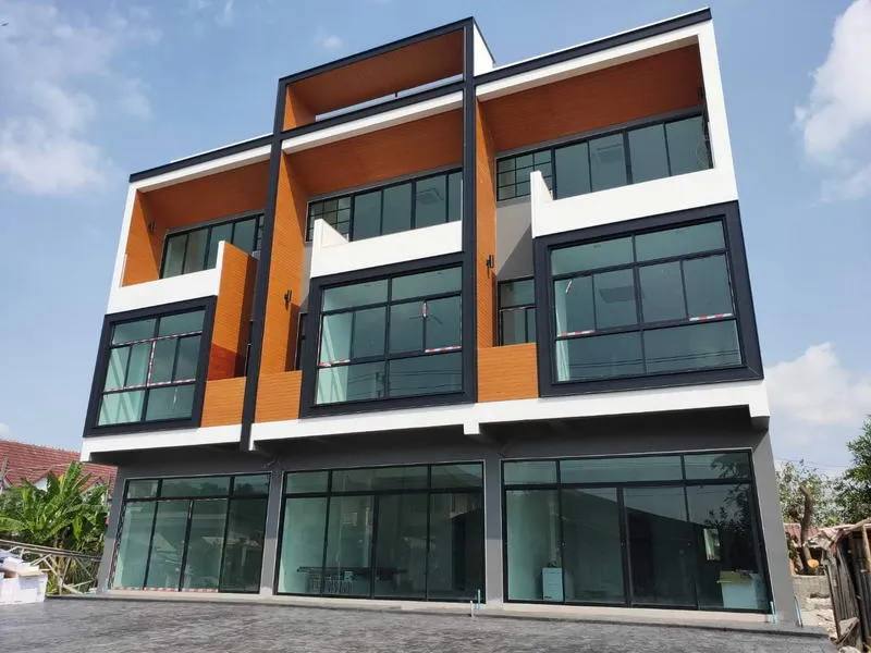 Three-story modern building with large windows, orange and black accents, and a paved foreground.