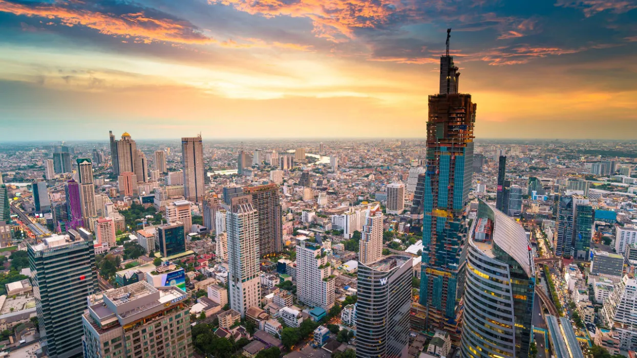 Bustling city skyline at sunset, with tall skyscrapers and a vibrant orange and blue sky.