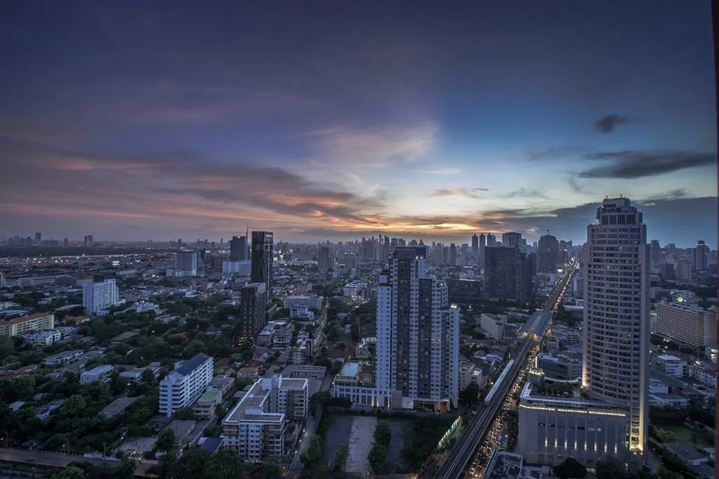 ภาพทิวทัศน์เมืองยามพลบค่ำ ที่มีตึกสูงระฟ้า ถนนสว่างไสว และท้องฟ้าสีสันสดใสยามพระอาทิต
