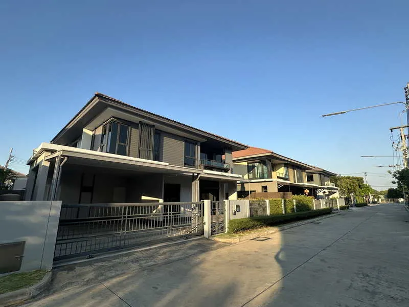 Modern two-story house with a gated entrance, located on a quiet residential street, under a clear blue sky.