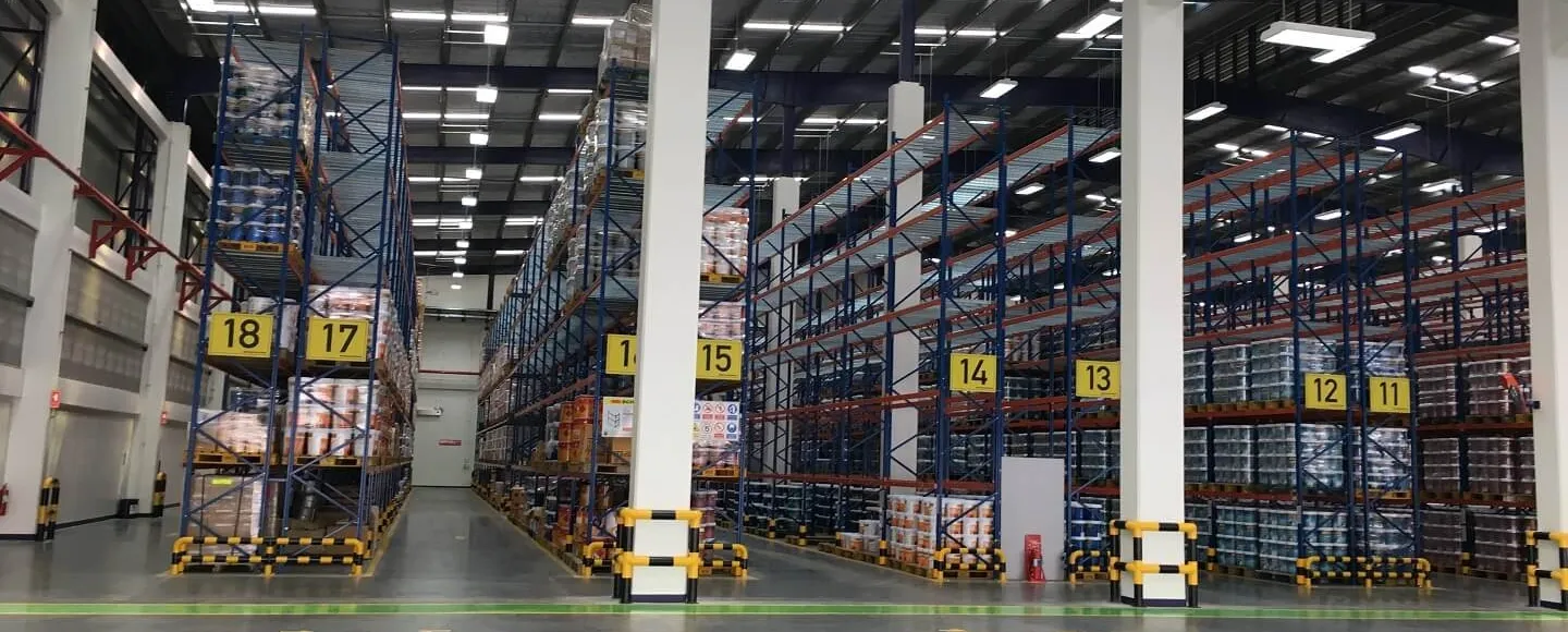 Warehouse interior with high shelves, numbered 18 to 11, stocked with various goods. The space is well-lit with a visible pathway between the shelves.