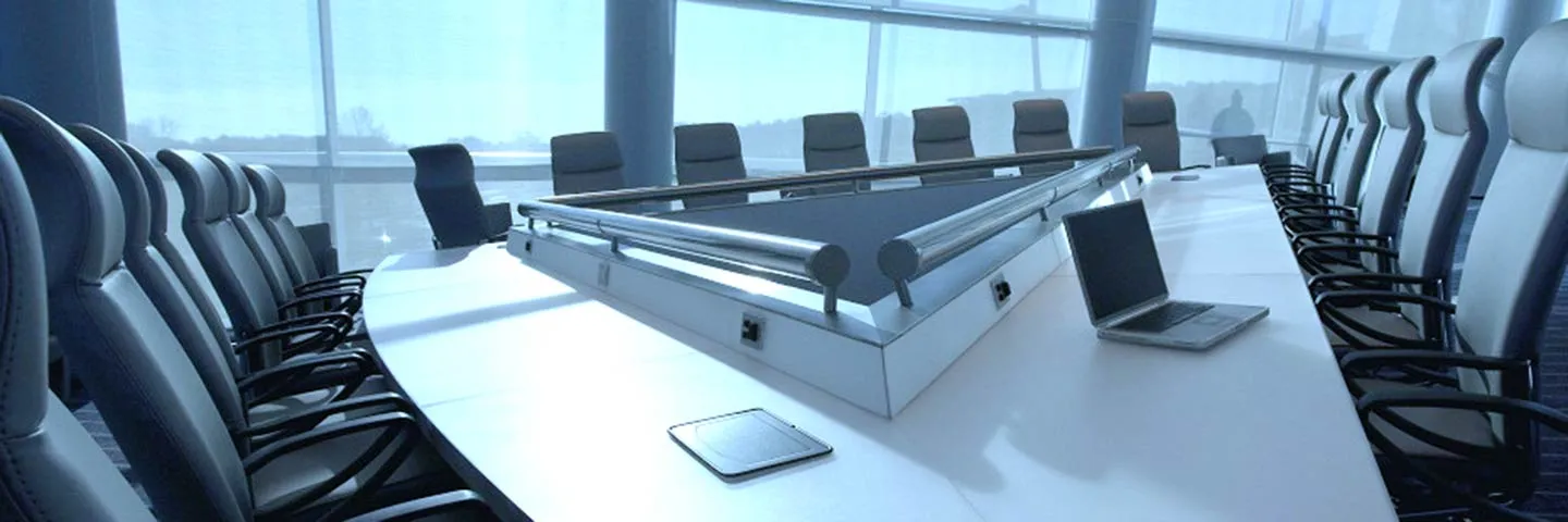 Large conference room with a triangular white table surrounded by black and white chairs, and a laptop placed on the table.