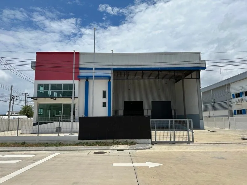 A modern industrial building with a red and white facade, featuring large garage doors and a gated driveway under a partly cloudy sky.