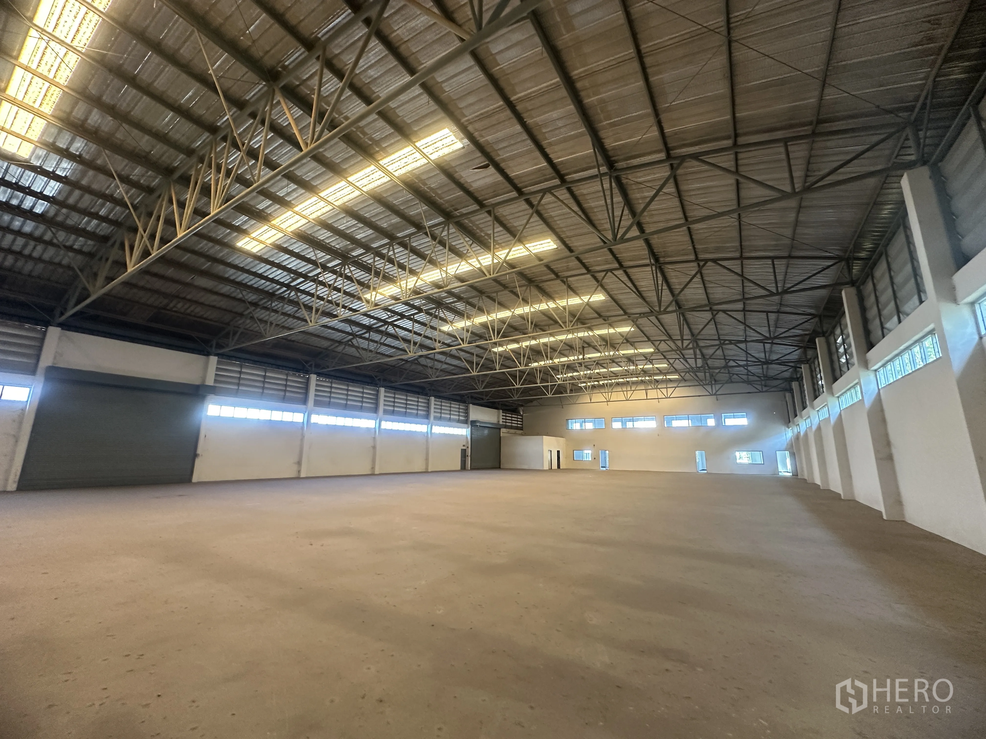 Factory for rent in Bang Pa-in, Phra Nakhon Si Ayutthaya - Wide warehouse interior showing open span roof structure, bright lighting, and a roller shutter door.