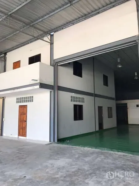 Factory for rent in Bang Phli, Samut Prakan - High-ceiling factory bay with large roller shutter, mezzanine office and green epoxy floor.