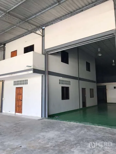 Factory for rent in Bang Phli, Samut Prakan - High-ceiling factory bay with large roller shutter, mezzanine office and green epoxy floor.