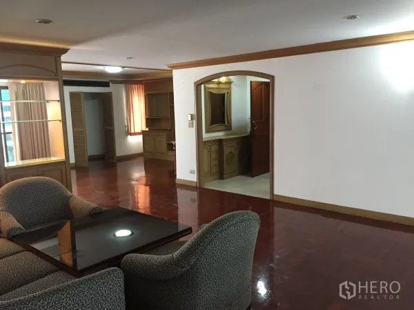Condominium for rent in Khlong Toei, Bangkok - Lounge with armchairs, arched doorway, display shelves, and polished hardwood flooring.