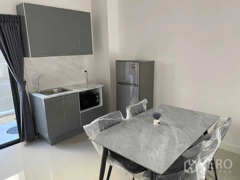Townhouse for rent in Prawet, Bangkok - Open-plan kitchen and dining zone with gray cabinets, fridge and four-seat table.