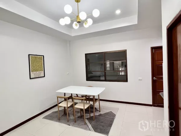 Townhouse for rent or sale in Phra Khanong, Bangkok - Bright dining room with a modern chandelier, white table, and four wooden chairs.