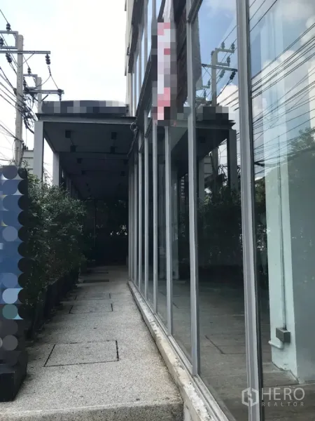 Retail Space for rent in Watthana, Bangkok - Side walkway beside a floor-to-ceiling glass storefront with planters and an overhead canopy.
