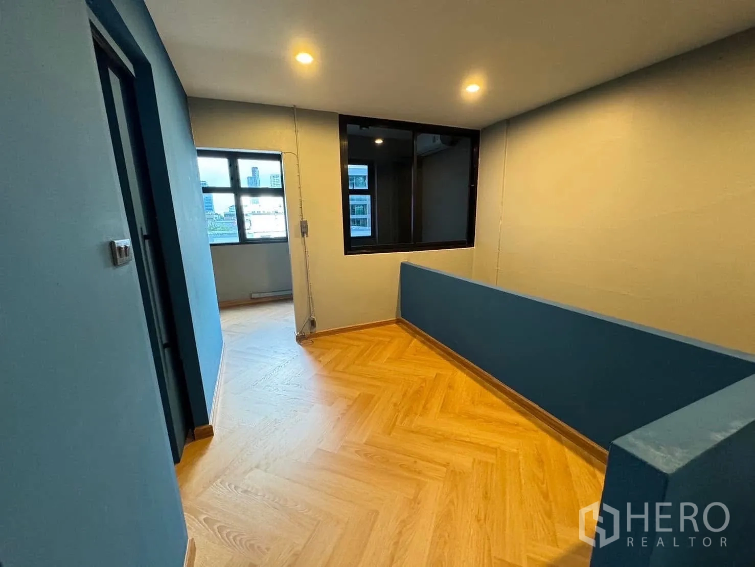 Home Office for rent in Watthana, Bangkok - Upper hallway with herringbone wood floor and a windowed interior partition.