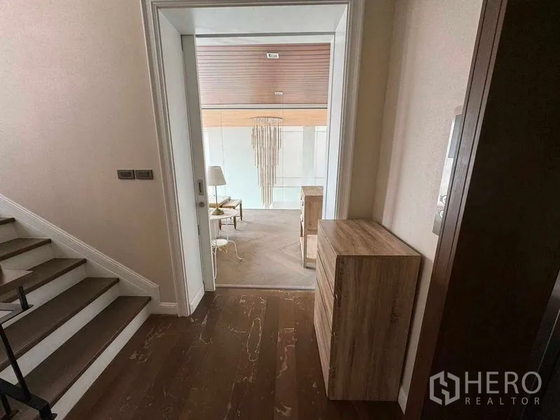 Townhouse for rent in Watthana, Bangkok - Hallway by the stairs opening to a lounge area with wood floors and pendant feature.