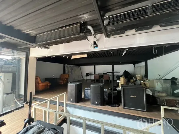 Retail Space for rent - Raised stage area inside an industrial-style retail space with speakers, leather lounge chairs, and a side glass wall.