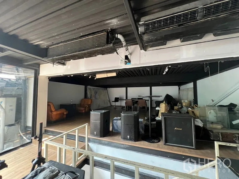 Retail Space for rent - Raised stage area inside an industrial-style retail space with speakers, leather lounge chairs, and a side glass wall.