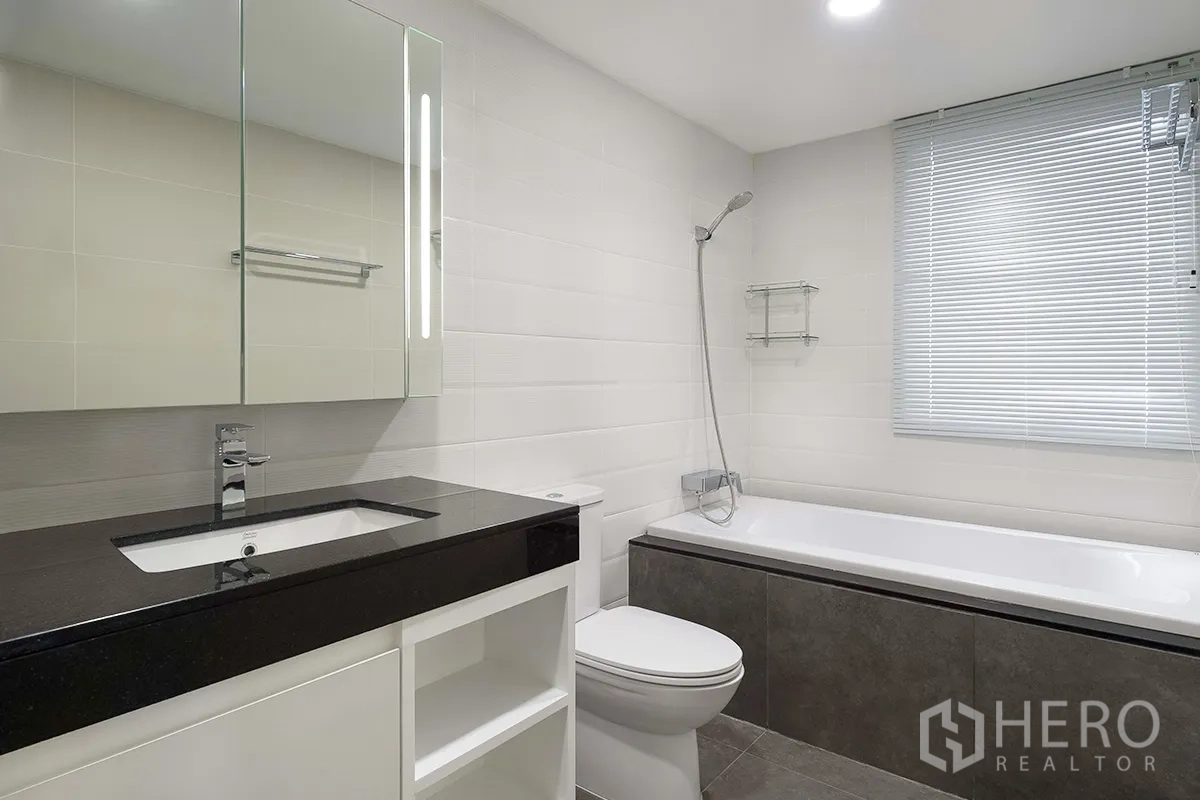 公寓 for rent in Khlong Toei, Bangkok - 明亮的浴室，设有浴缸、淋浴、黑色台面洗手台与百叶窗。