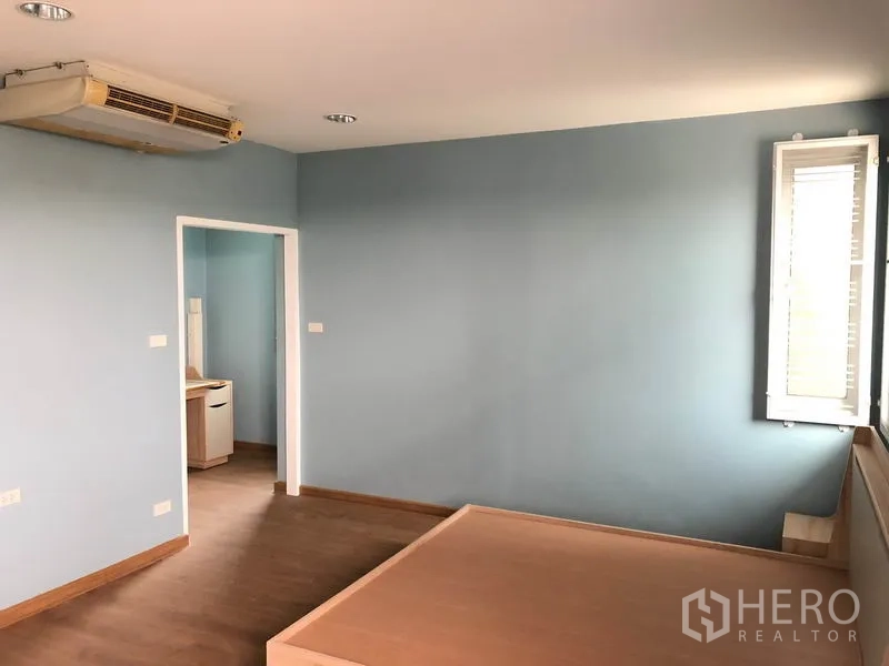 Detached House for sale in Bang Khen, Bangkok - Bedroom with platform bed, blue walls, corner window and door to dressing or bathroom area.