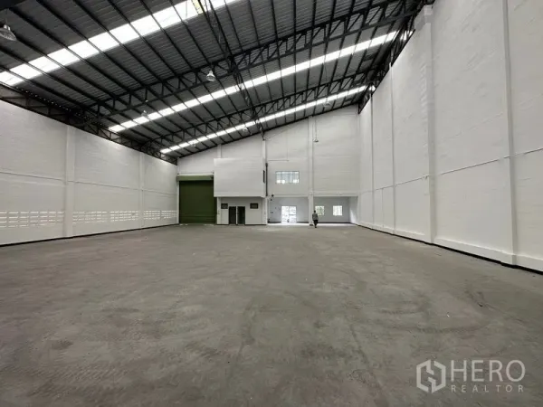 工厂 出租在Khlong Luang, Pathum Thani - 厂房内展示宽幅绿色装卸门、夹层办公区与打磨混凝土地面。
