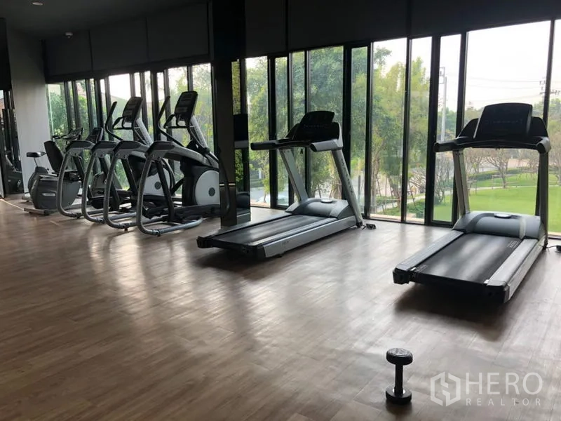 Detached House for rent or sale in Bang Kapi, Bangkok - Fitness room with treadmills and ellipticals facing large windows and garden views.