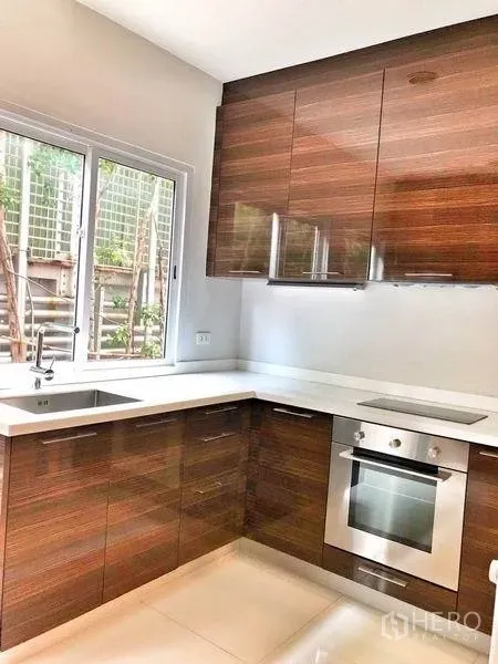 Townhouse for rent in Watthana, Bangkok - L-shaped western kitchen with wood cabinets, oven, and a window.