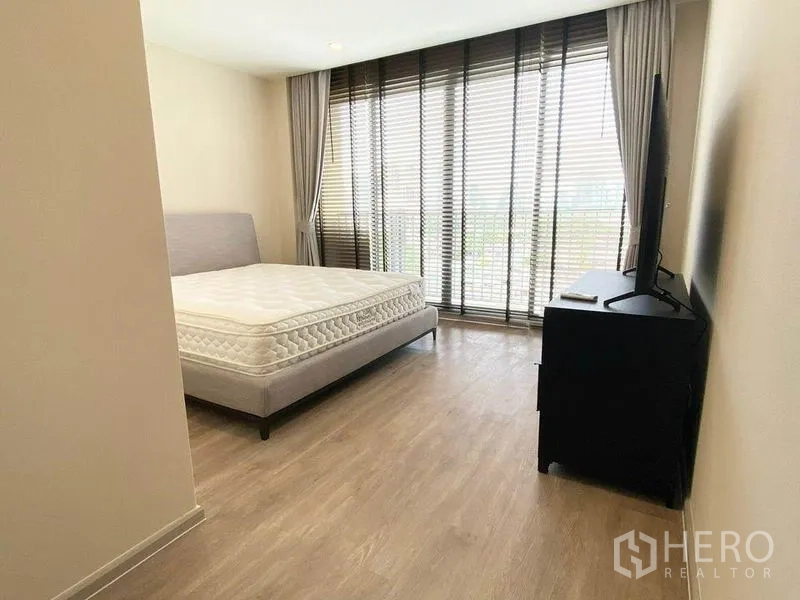 Condominium for rent in Pathum Wan, Bangkok - Spacious master bedroom with wood floors, TV on dresser and full-height windows opening to a balcony.