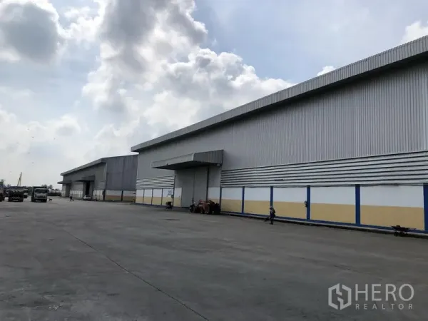 Warehouse for rent in Phra Nakhon Si Ayutthaya - Wide concrete yard facing long steel-clad warehouse blocks under a cloudy sky in Bang Sai.