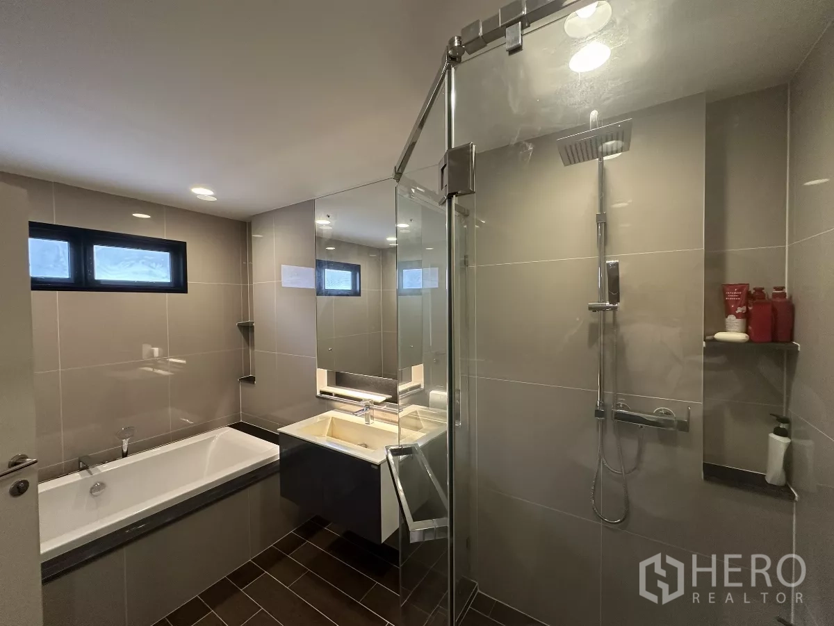Detached House for rent or sale in Lam Luk Ka, Pathum Thani - Modern bathroom with glass-enclosed rain shower, bathtub, vanity and large mirror.