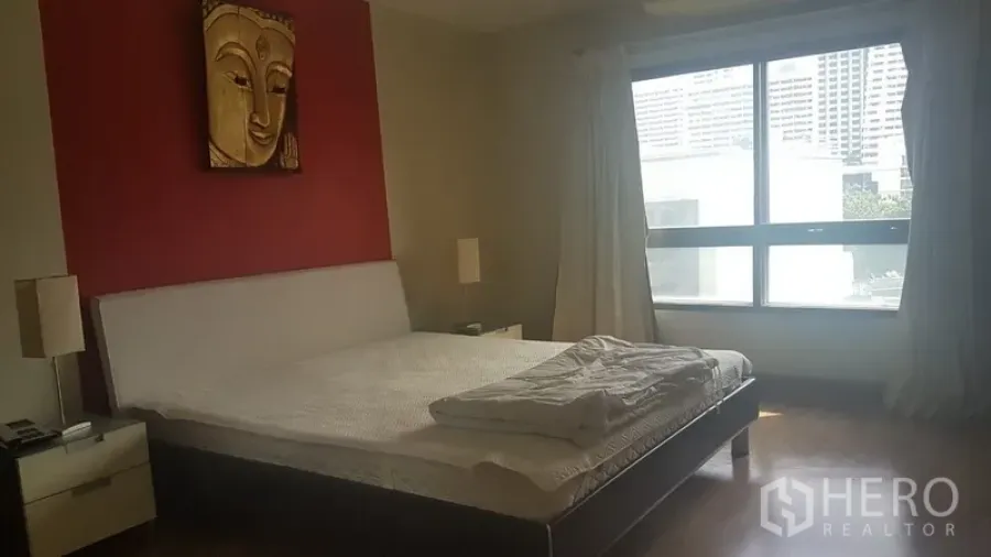 Condominium for rent in Pathum Wan, Bangkok - Spacious bedroom with red accent wall, large window with curtains, wood flooring and a double bed.