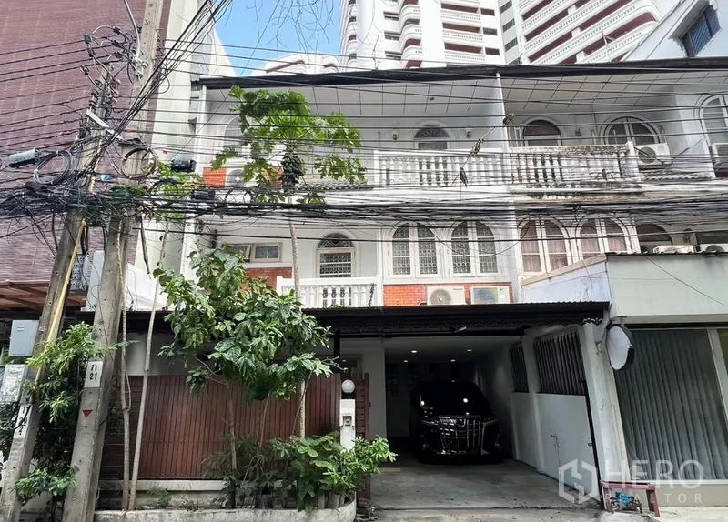 Townhouse for rent in Khlong Toei, Bangkok - Three-storey townhouse facade with arched windows, classic railings and a covered carport in a city setting.