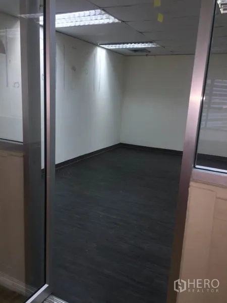 Office Space for rent in Watthana, Bangkok - Empty office room with glass partition, dark wood flooring, white walls and fluorescent ceiling lights.