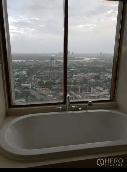 Condominium for rent - Soaking bathtub set by a large window showcasing a panoramic city skyline view.