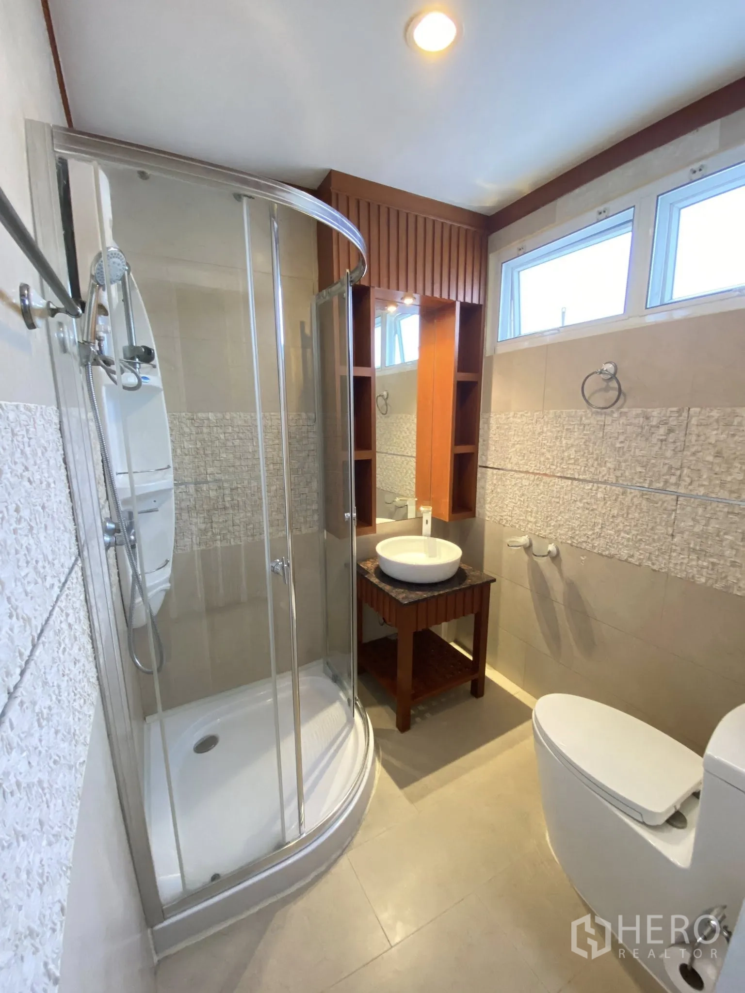 Home Office for rent in Pathum Wan, Bangkok - Compact bathroom with curved glass shower enclosure, vessel sink, and upper windows.
