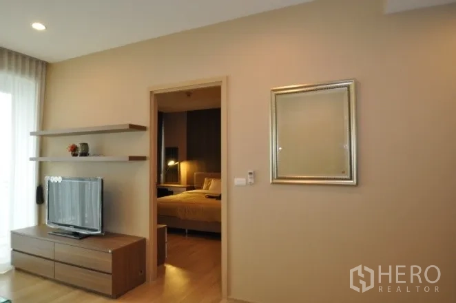 Condominium for rent or sale in Watthana, Bangkok - Living room with TV console, wall shelves, and doorway to bedroom.