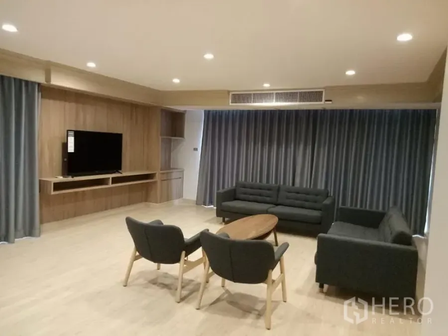 Apartment for rent in Khlong Toei, Bangkok - Living room with grey sofas, TV wall and floor-to-ceiling curtains