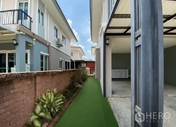 Detached House for rent in Suan Luang, Bangkok - Narrow side yard with artificial turf and plants beside the covered parking and service counter.