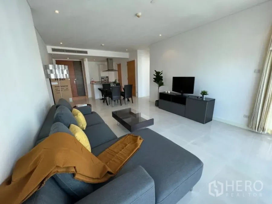 Condominium for rent or sale in Watthana, Bangkok - Spacious open-plan living room with gray sectional sofa, TV console, dining set and open kitchen.
