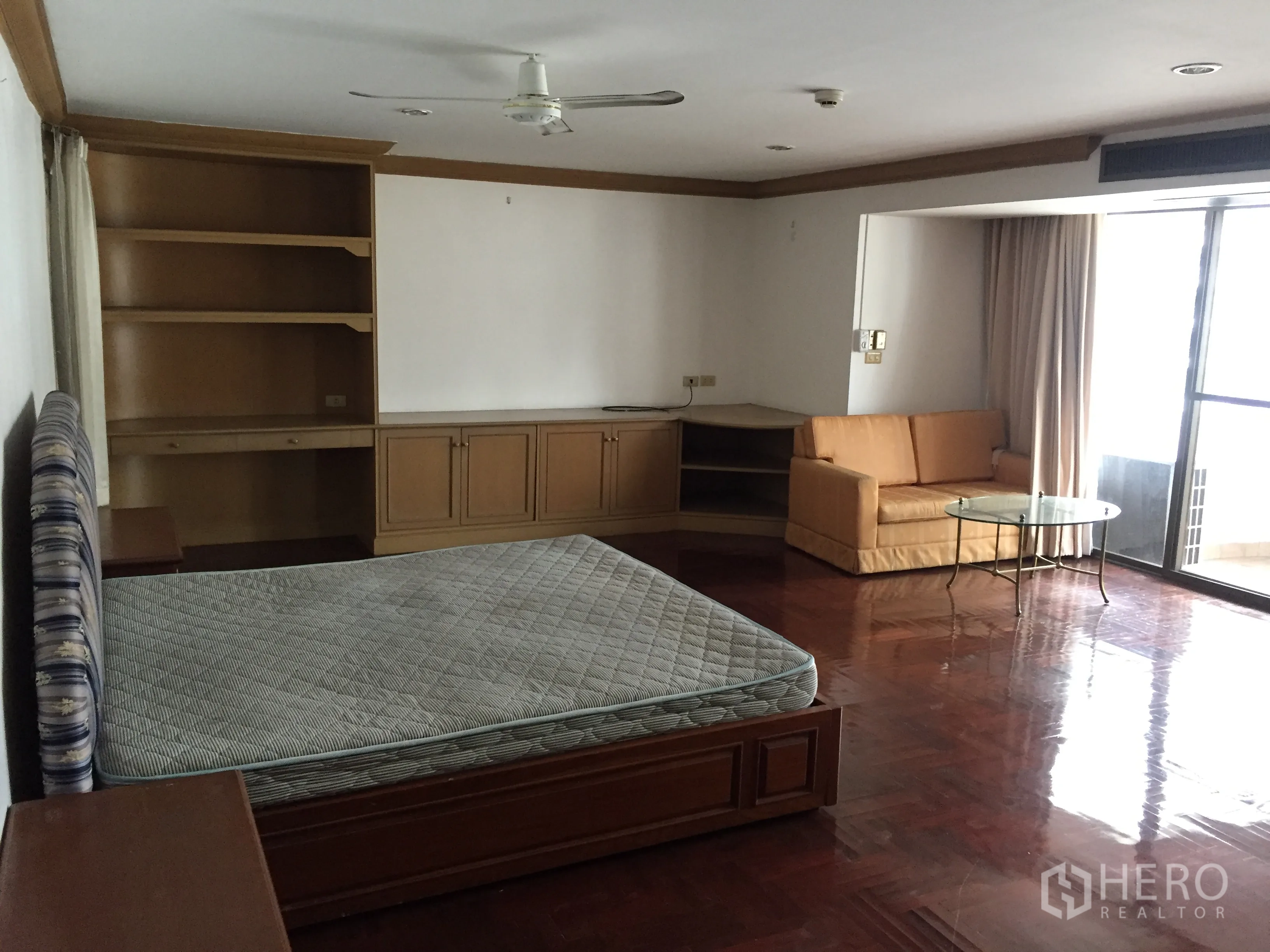 Condominium for rent in Khlong Toei, Bangkok - Master bedroom with balcony access, sofa corner, ceiling fan, and built-in storage.