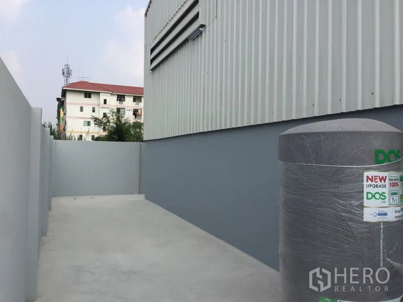 Warehouse for sale in Khlong Luang, Pathum Thani - Paved side yard with a water storage tank next to the warehouse wall.