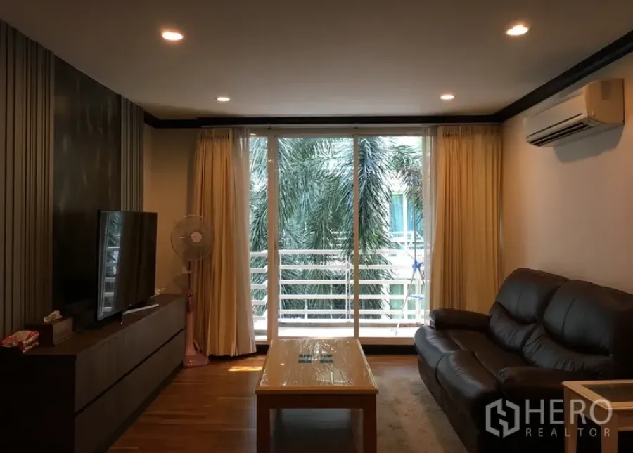 Condominium for sale in Khlong Toei, Bangkok - Bright living room with leather sofa, TV console and sliding doors opening to a balcony with palm views.