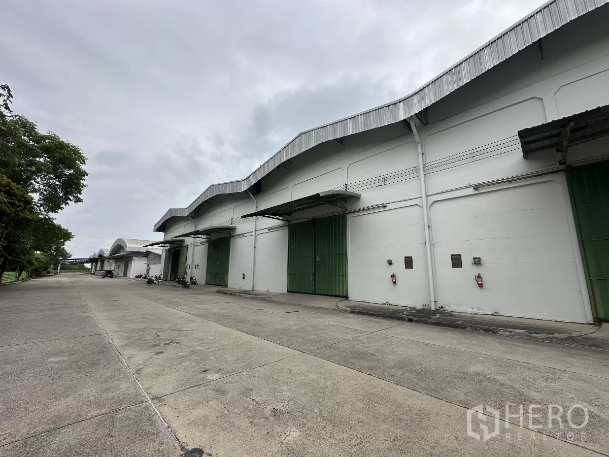 Warehouse for rent in Bang Pa-in, Phra Nakhon Si Ayutthaya - Row of white warehouses with green loading doors and a wide concrete driveway inside a secure compound.