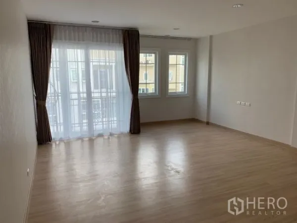 Townhouse for rent in Bang Na, Bangkok - Spacious bedroom with wood flooring, balcony door and corner windows with curtains