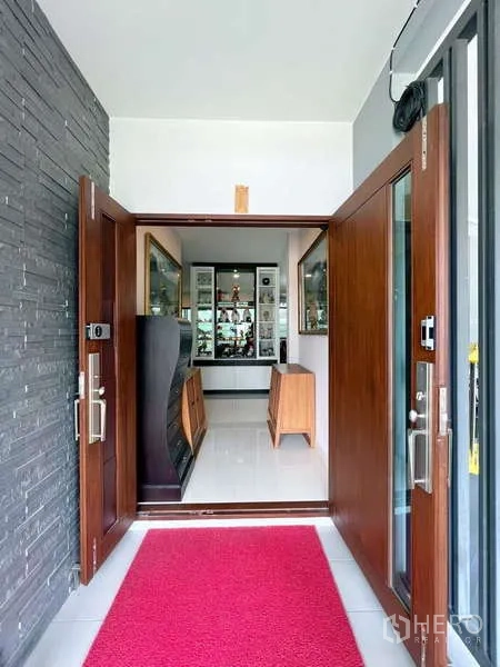 Detached House for sale in Prawet, Bangkok - Wide wooden front doors opening to a bright foyer with glass display cabinets and glossy floors.