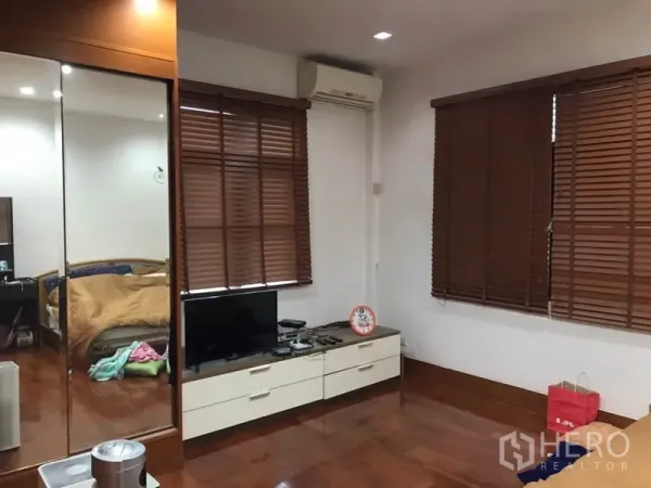 Detached House for sale in Lat Phrao, Bangkok - Bedroom or TV lounge with mirrored wardrobe, wooden blinds, air conditioner and polished timber floor.